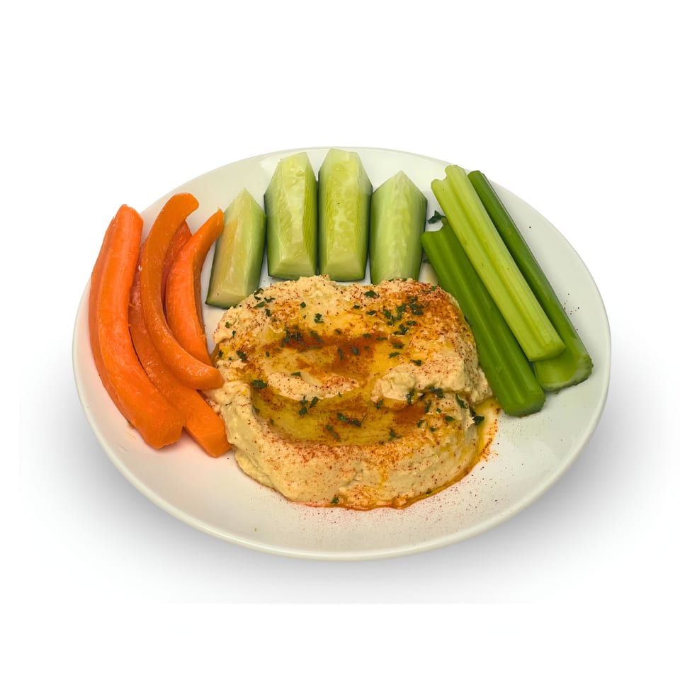 Hummus with olive oil and paprika, served with carrot sticks, cucumber spears, and celery on a white plate.