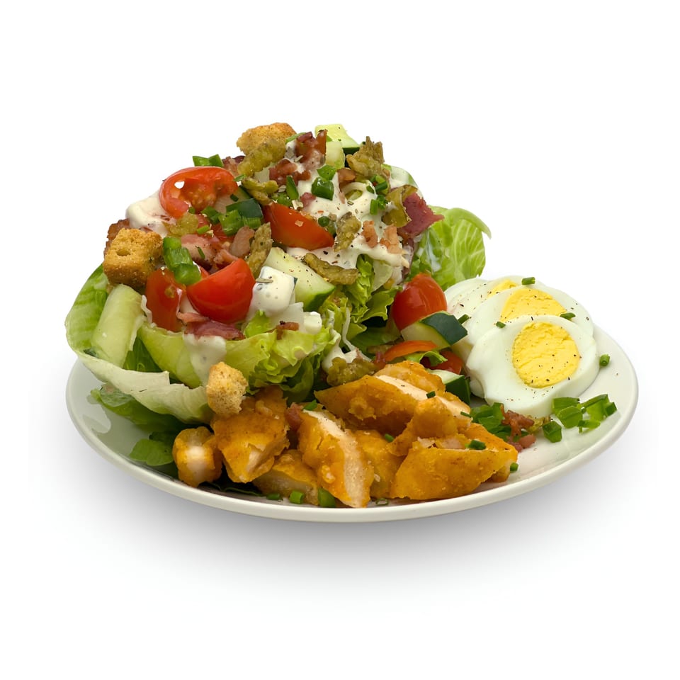 Wedgies salad with fried chicken, hard-boiled eggs, bacon, tomatoes, and croutons on a white plate.