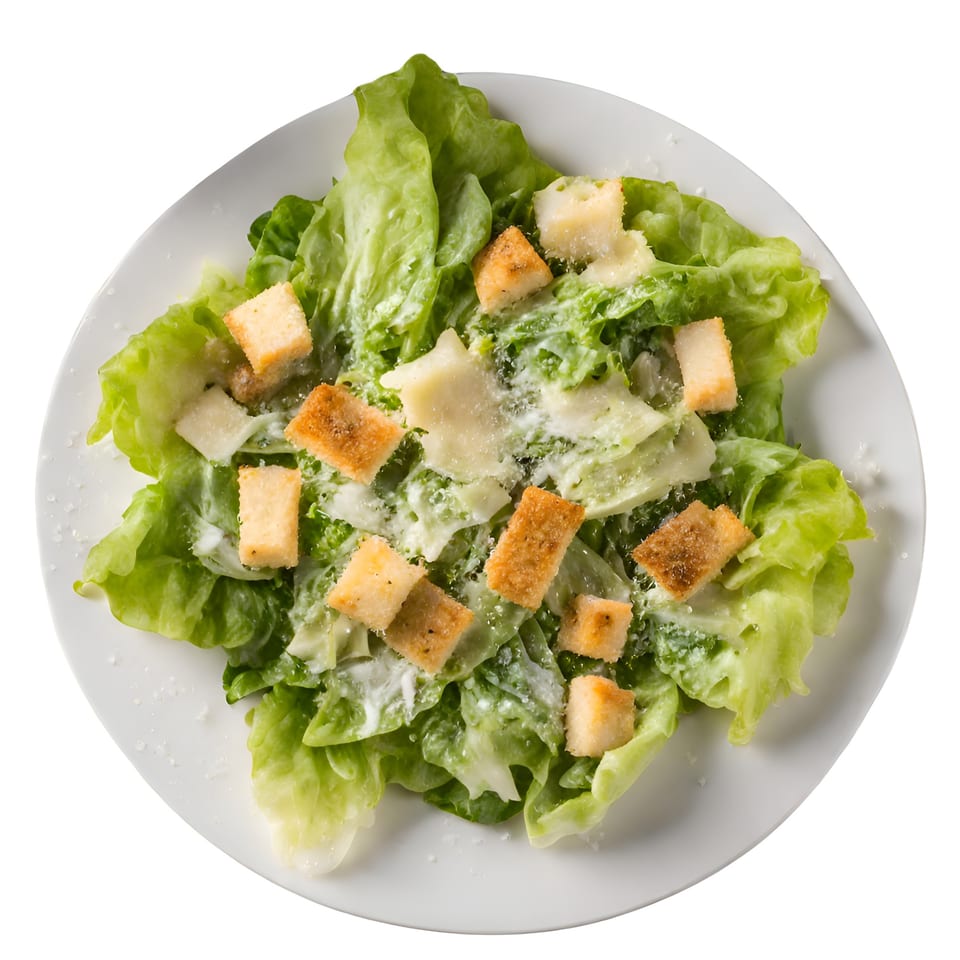 Overhead view of a Caesar salad with green lettuce, croutons, and parmesan cheese on a white plate.
