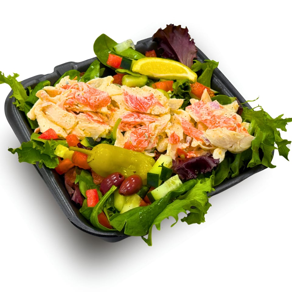 Wedgies' crab salad with lettuce, cucumber, tomatoes, olives, and a lemon wedge in a black container.