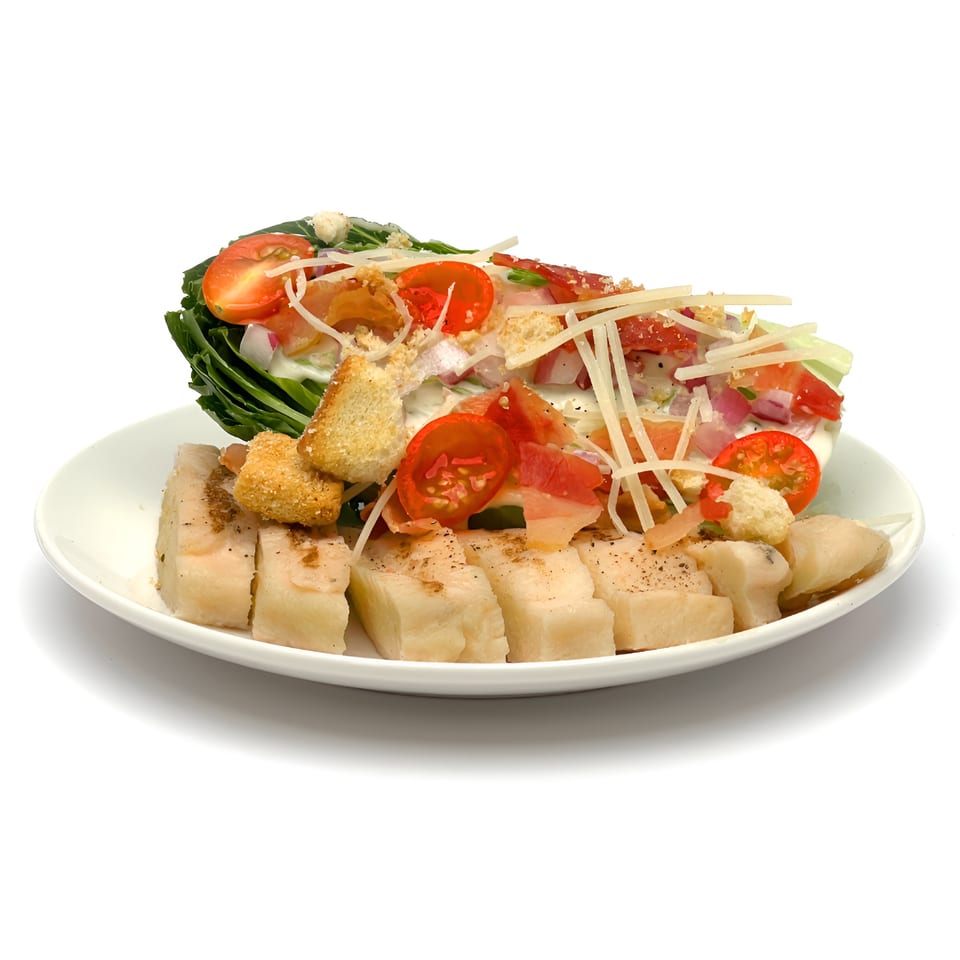 Wedgies salad with greens, tomatoes, croutons, cheese, and sliced chicken on a white plate.